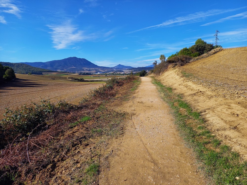 Hiekkatie Camino Frances pyhiinvaellusreitillä, taustalla vuoria ja espanjalainen kylä.