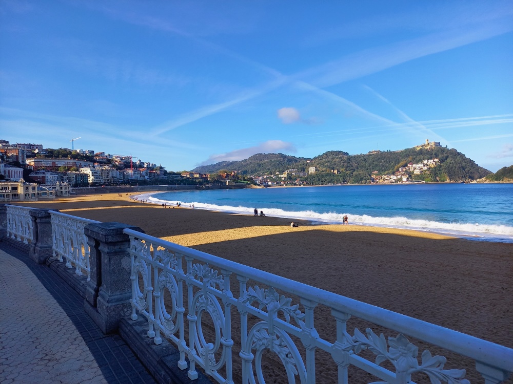 Hiekkaranta ja meri espanjalaisen kaupungin edustalla, taustalla vehreitä kukkuloita.