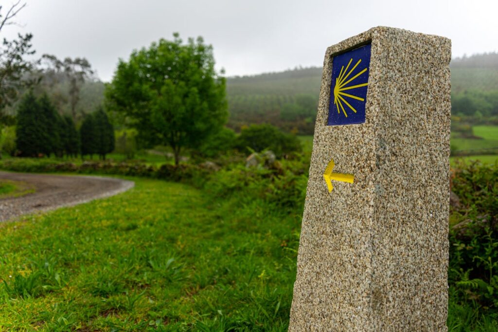 Camino de Santiago pyhiinvaelluksen reittimerkki Espanjassa. Reittimerkissä on keltainen nuoli ja simpukkatunnus sinisellä pohjalla.