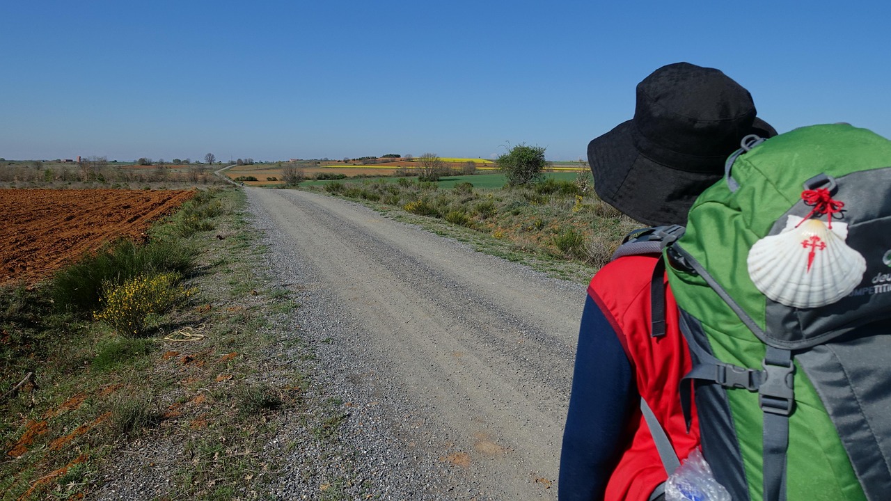 Vaeltaja Espanjan maaseudulla Camino de Santiago pyhiinvaellusreitillä selässään reppu, johon kiinnitettynä pyhiinvaelluksen simpukkatunnus.